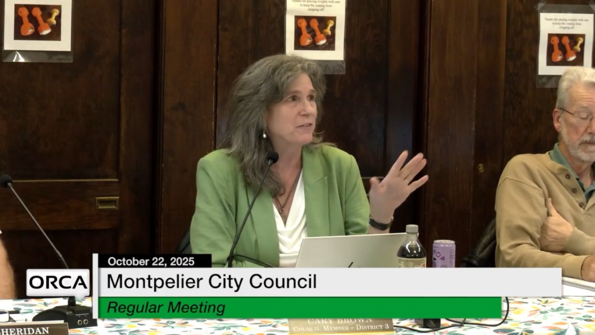 A woman in a green blazer speaks at a table during the Montpelier City Council regular meeting on October 22, 2025.