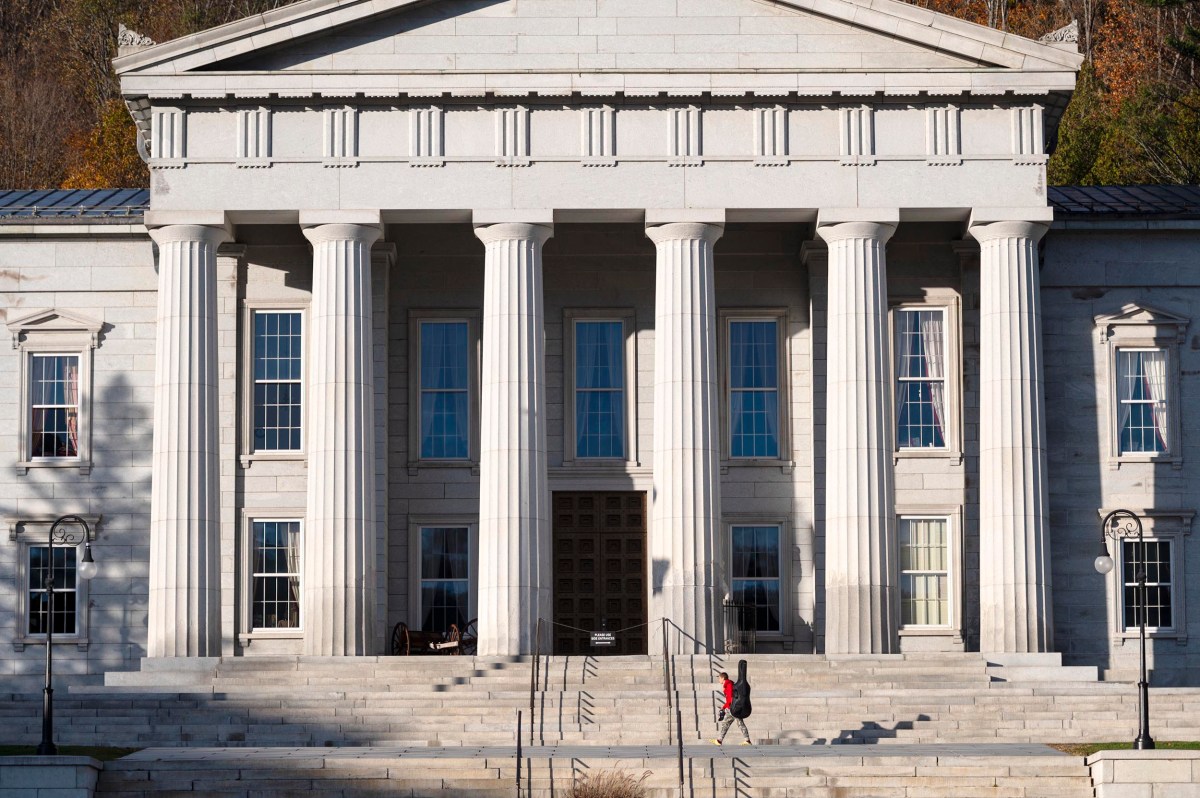 A neoclassical building with large columns and wide steps; a person in red walks up the stairs toward the entrance.