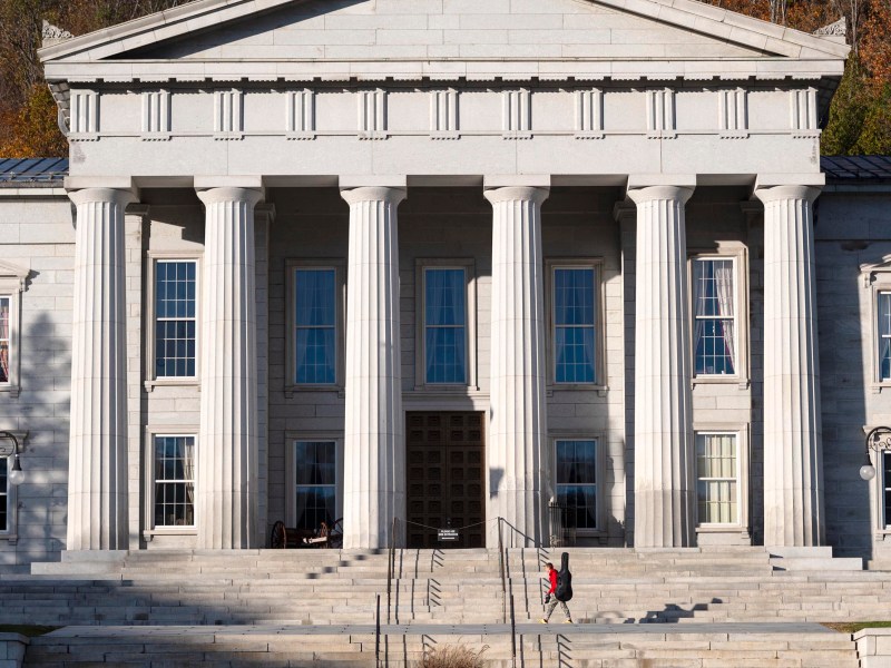 A neoclassical building with large columns and wide steps; a person in red walks up the stairs toward the entrance.