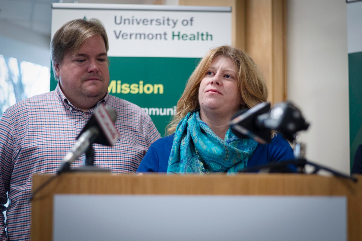 Two people stand at a podium with microphones, in front of a University of Vermont Health sign during a press event.