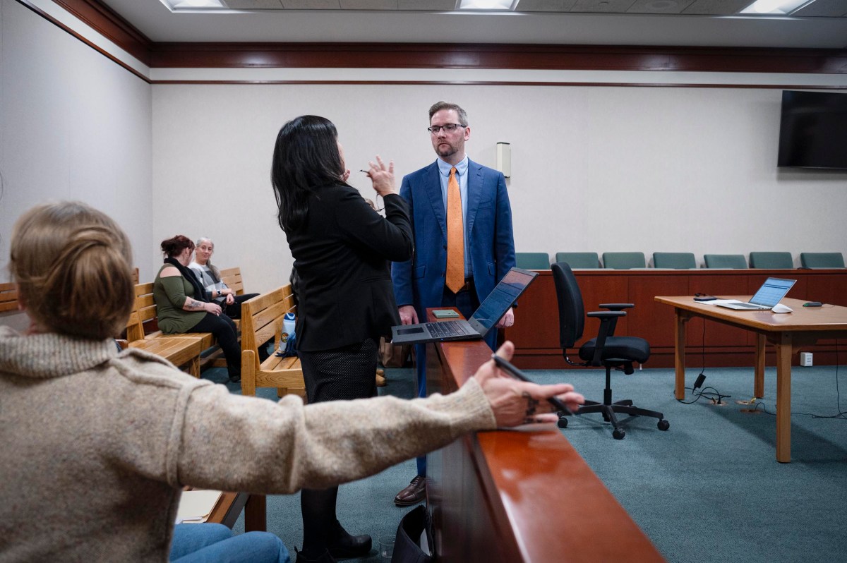 A man in a suit stands facing a woman who is gesturing, while another person in the foreground points toward them in a courtroom setting.