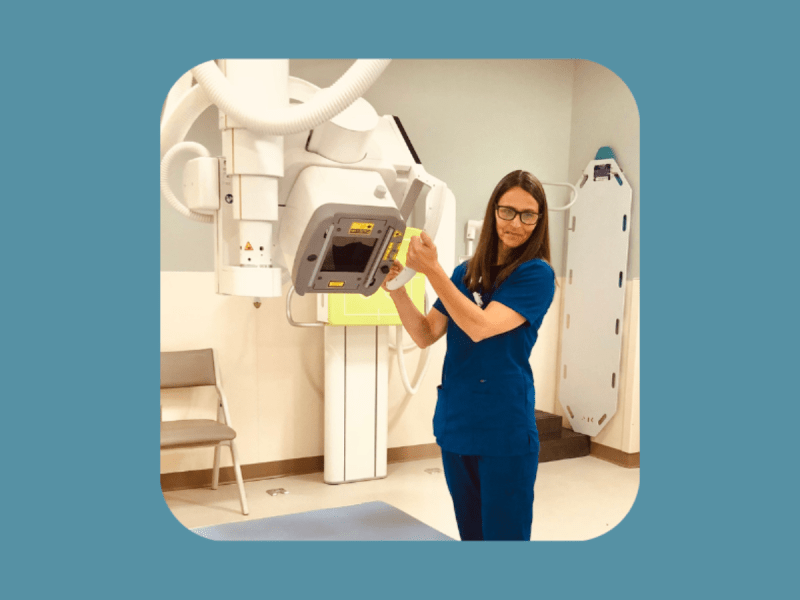 A healthcare professional in blue scrubs adjusts an X-ray machine in a medical imaging room.