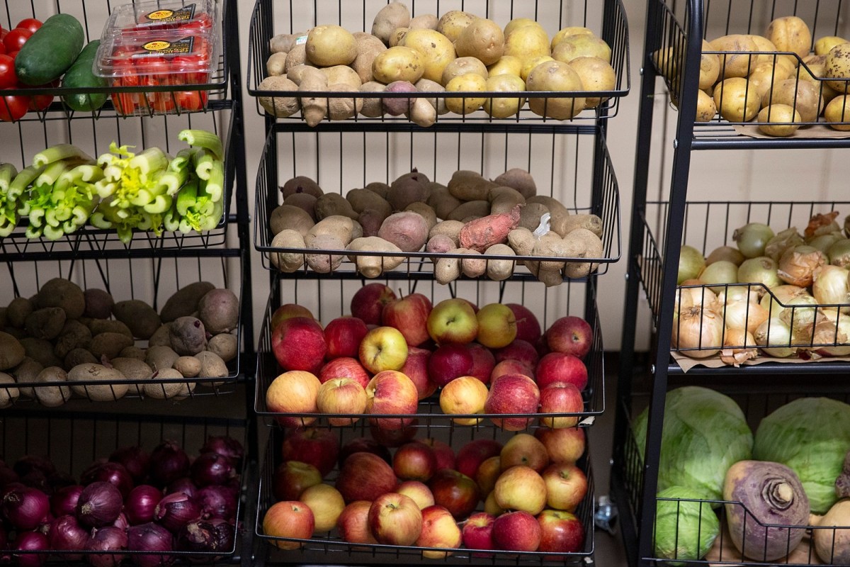 Metal shelves filled with assorted vegetables and fruits including apples, potatoes, onions, peppers, cabbage, and turnips.