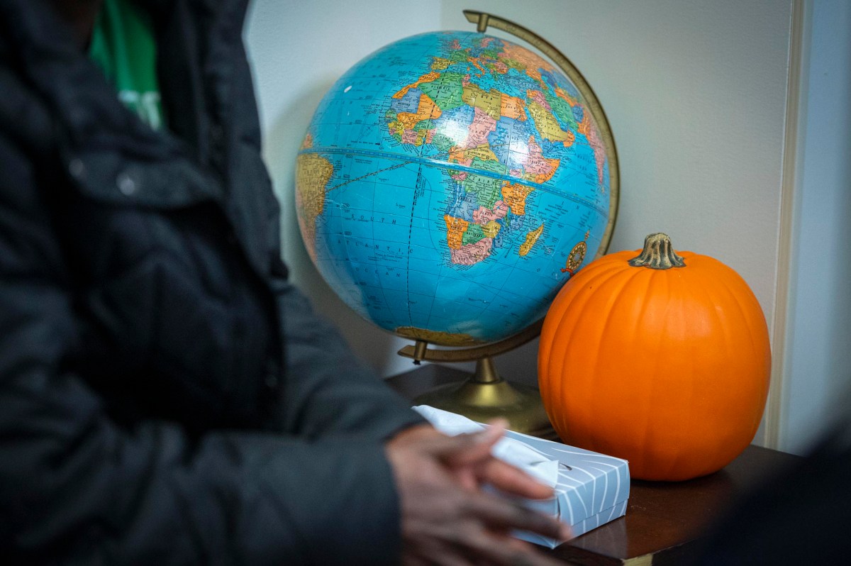 A globe and an orange pumpkin sit on a table next to a box of tissues, with a person partially visible in the foreground.