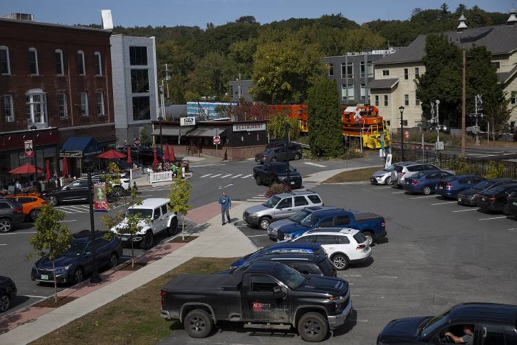 A parking lot with several cars in front of shops and restaurants; construction vehicles and trees are visible in the background.