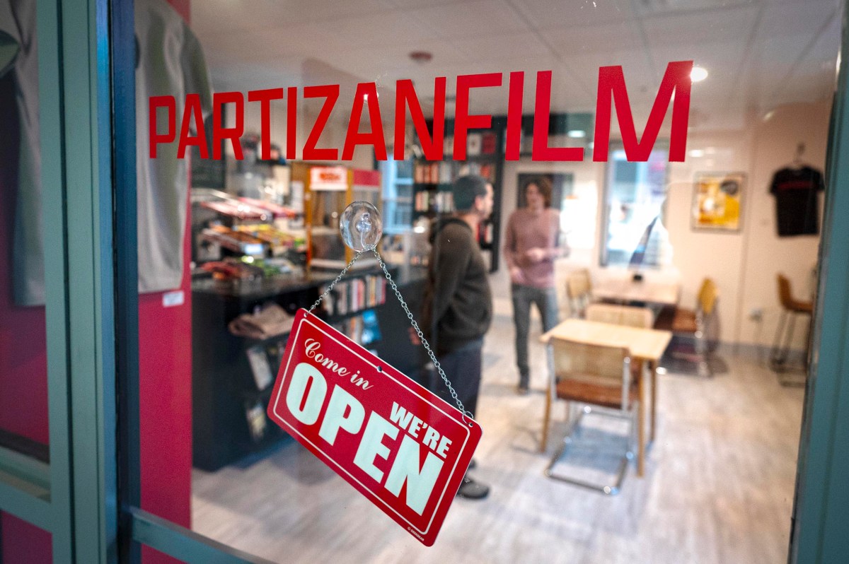 Glass door with a "Come in, we're open" sign and "PARTIZANFILM" written above; two people stand inside a modern office space.