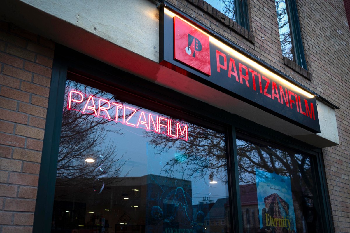 Storefront with a neon "PARTIZANFILM" sign and a backlit sign above the window displaying the same name and a red logo featuring a drop symbol.