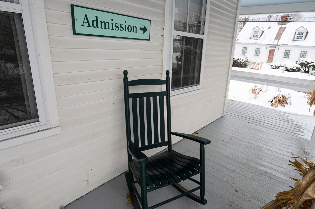 A green rocking chair sits on a gray wooden porch near a sign reading "Admission" with an arrow pointing right.