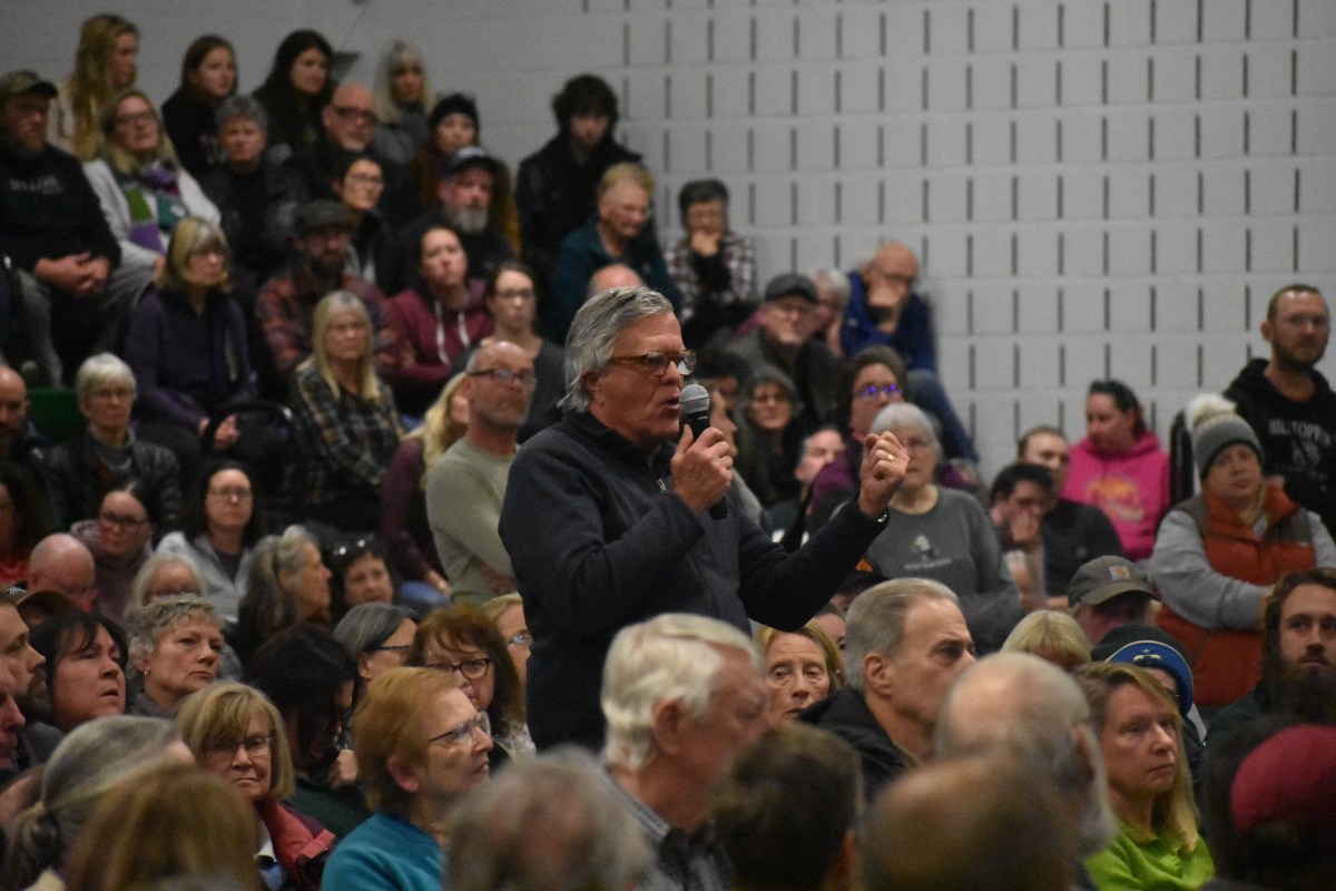 A man speaks into a microphone in front of a crowd of people sitting in a school.