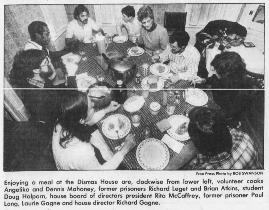 A group of ten people sits around a dining table sharing a meal at Dismas House, with plates and food visible.