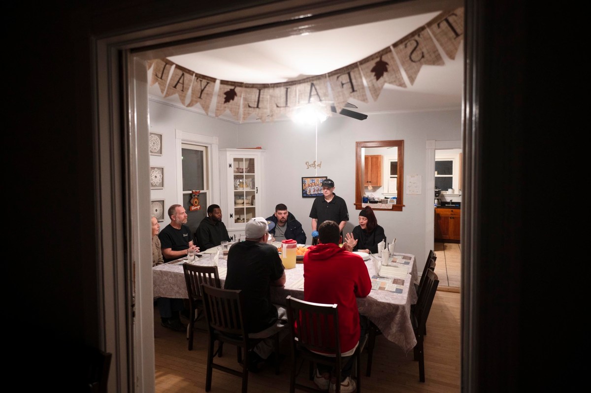 A group of people sit around a dining table in a home, having a meal together. A "It's Fall Y'all" banner hangs above them.