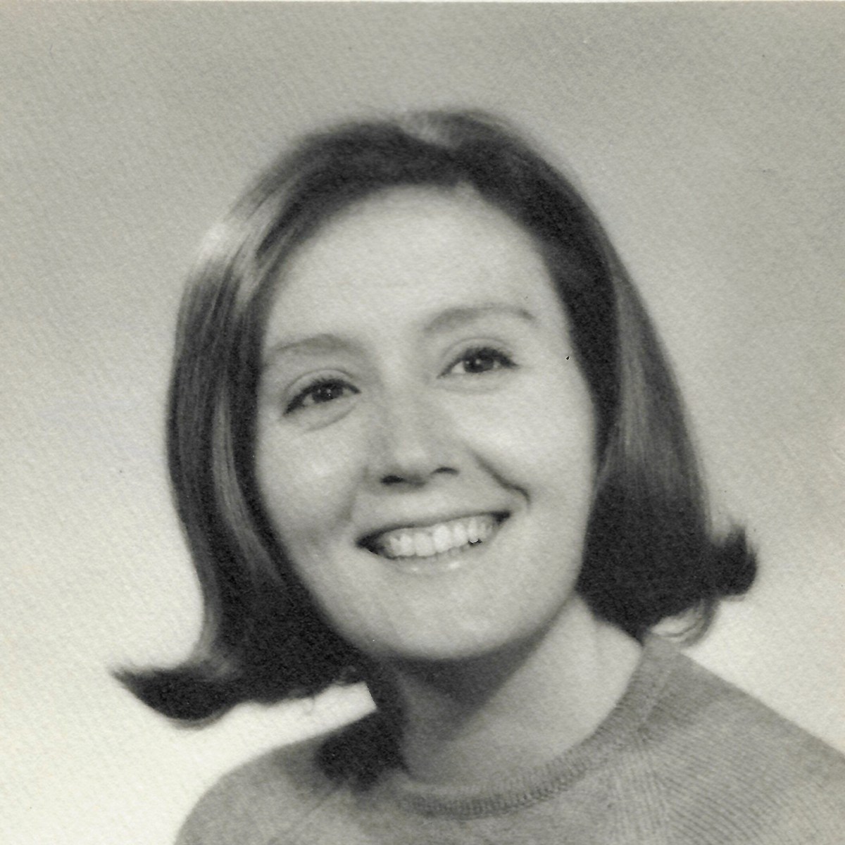 Black and white portrait of a woman with short, straight hair, smiling and wearing a light-colored sweater, set against a plain background.