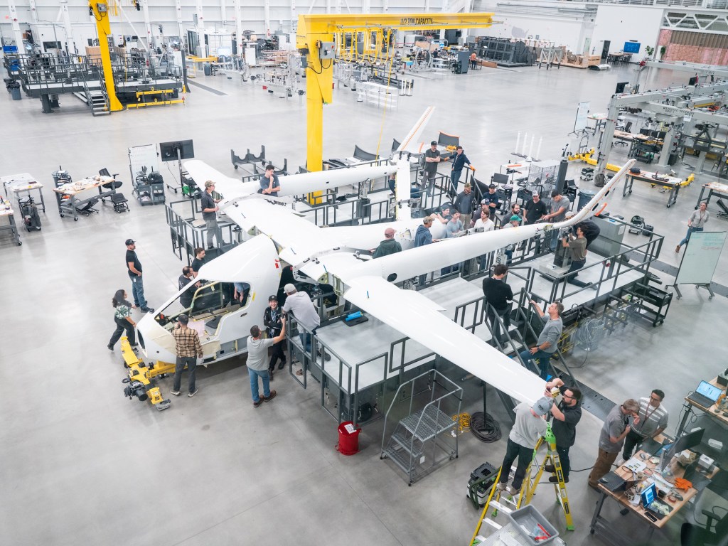 A group of people work together to assemble a large white drone aircraft in a spacious industrial workshop.