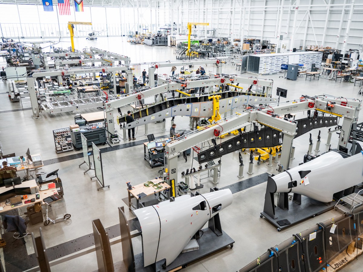 A large, clean aerospace manufacturing facility with machinery, assembly lines, and aircraft components under construction.