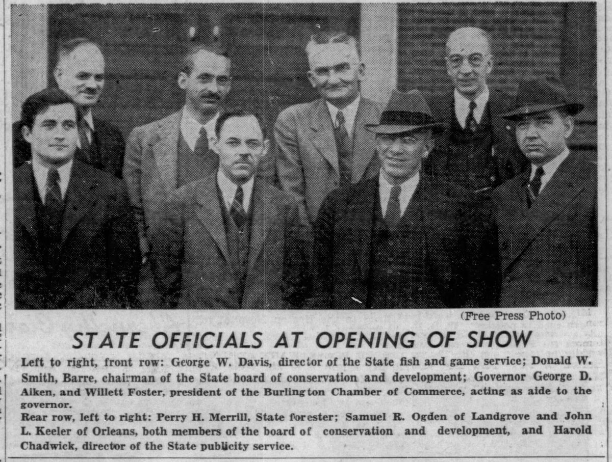 Eight male state officials standing in two rows, posing for a group photo at the opening of a show, all dressed in formal suits and ties.