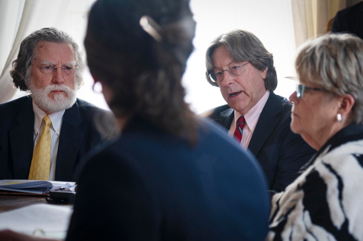 Four people in business attire sit around a table having a serious discussion, with papers and folders visible.