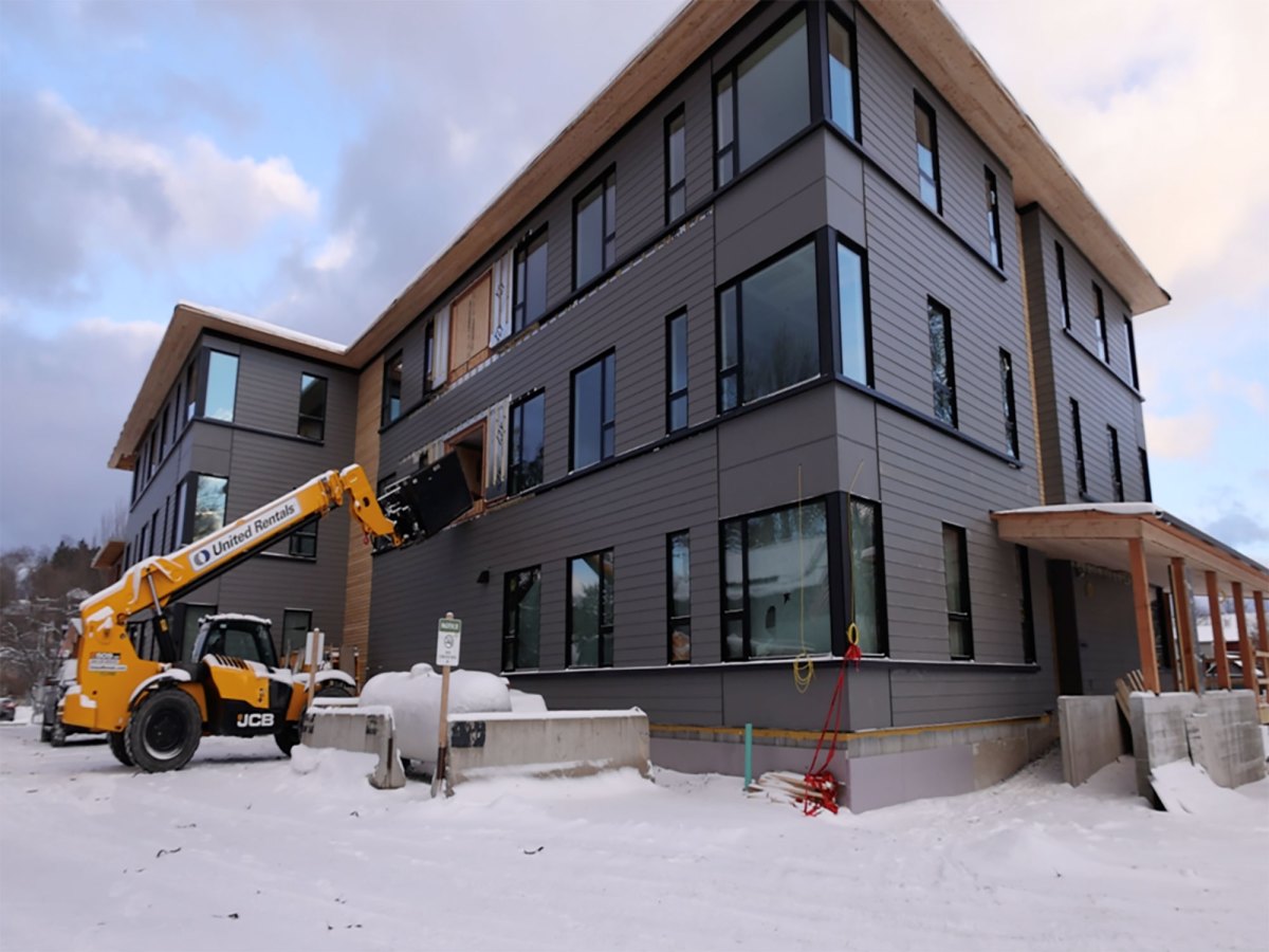 A construction vehicle is parked beside a three-story modern building with large windows on a snowy day.