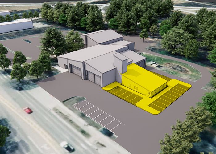 Aerial rendering of a building complex with a highlighted yellow section and parking spaces, surrounded by trees and adjacent to a road.