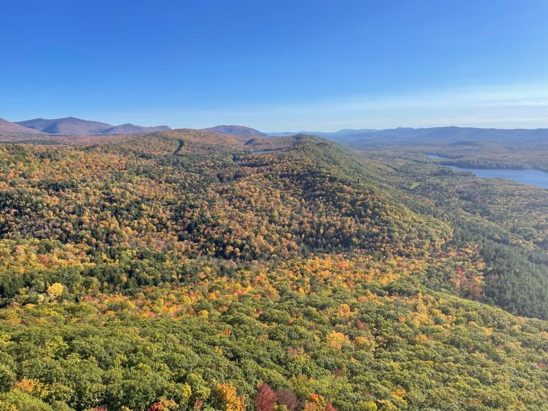 A wide view of rolling hills covered in autumn foliage with a lake to the right and a clear blue sky above.