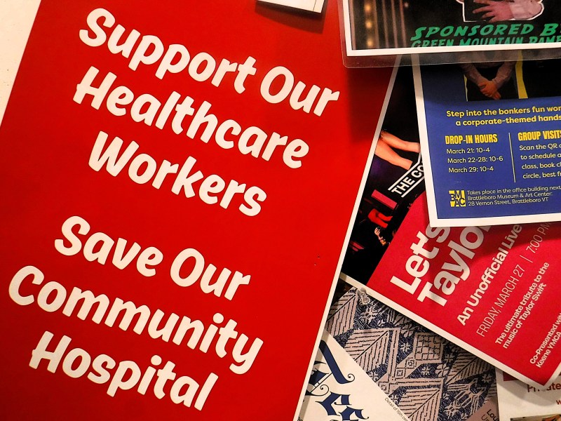 A red sign reads, "Support Our Healthcare Workers Save Our Community Hospital," surrounded by various colorful flyers and papers.