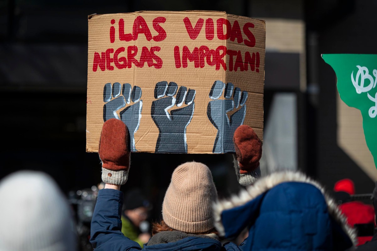 A person in winter clothing holds a cardboard sign reading "¡LAS VIDAS NEGRAS IMPORTAN!" with three raised fists painted below the text.