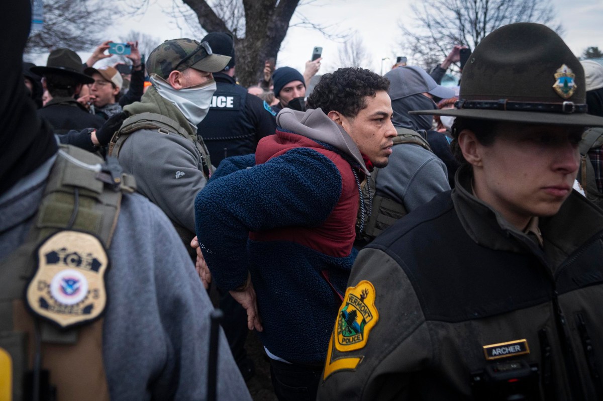 A man is handcuffed and escorted by police officers during a public event as bystanders take photos and videos.