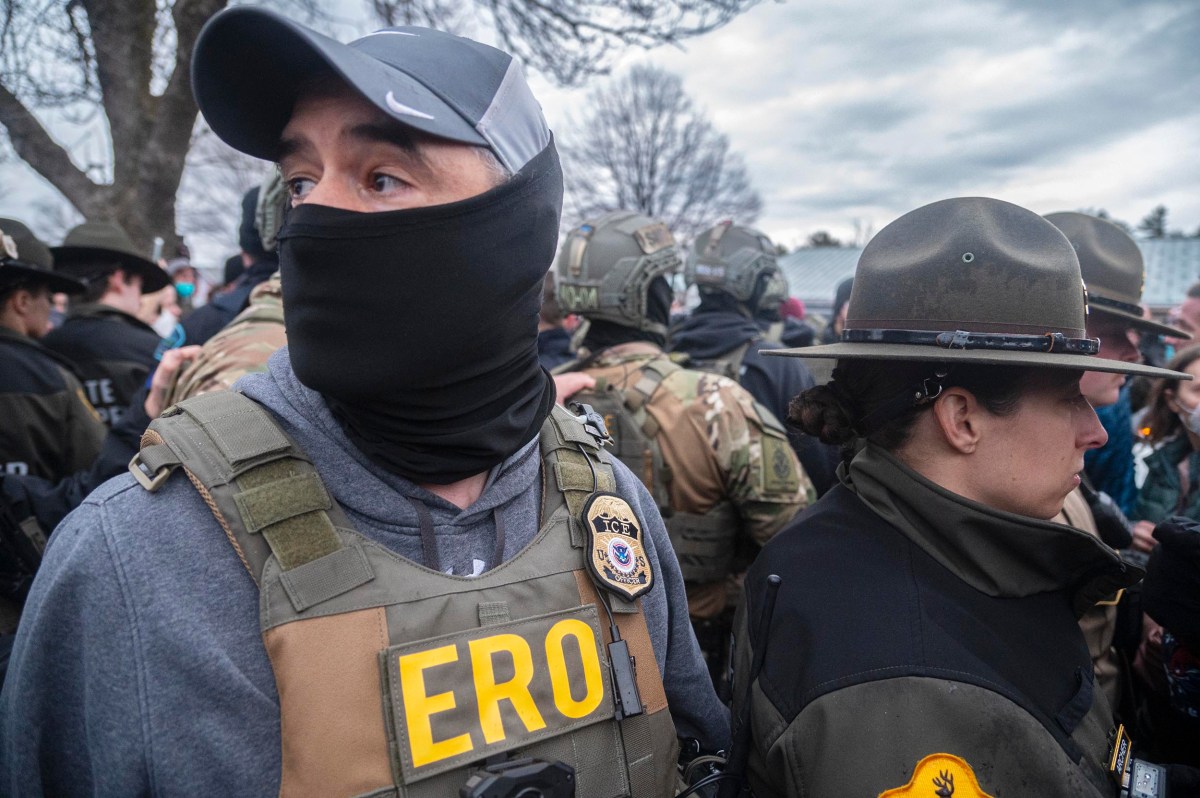 A group of law enforcement officers, some wearing tactical gear and ERO badges, stand closely together outdoors under a cloudy sky.