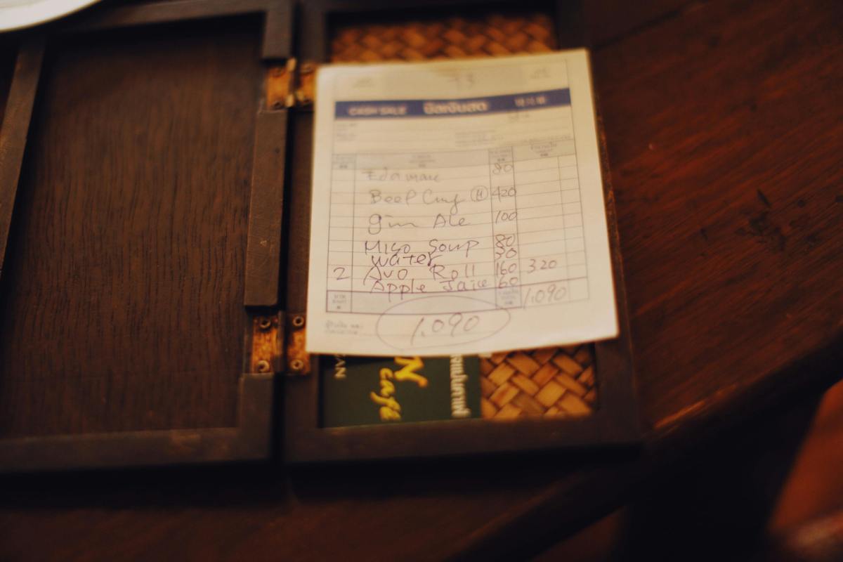A restaurant bill listing food and drink items with handwritten prices, totaling 1,090, placed on a dark wooden bill holder.