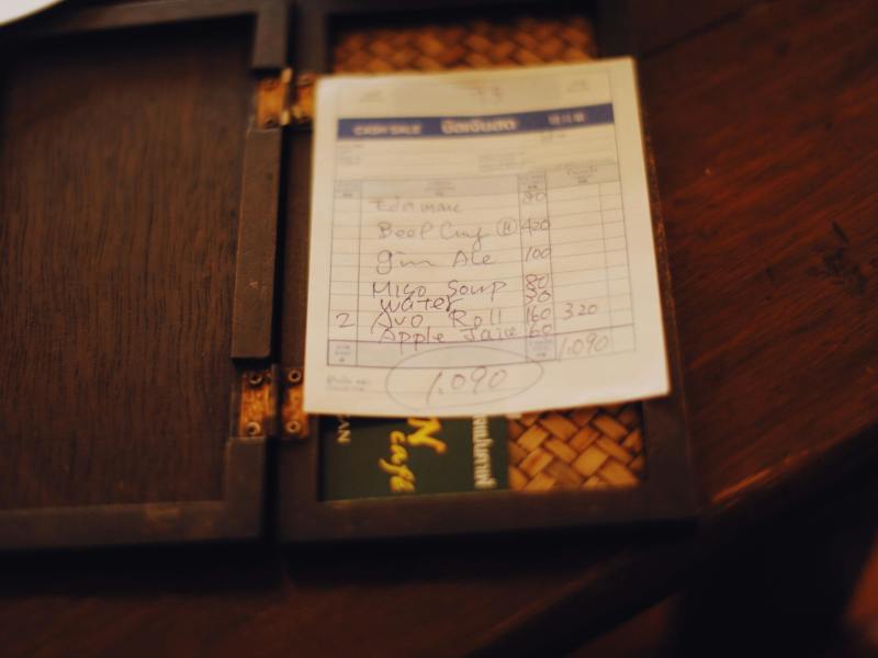 A restaurant bill listing food and drink items with handwritten prices, totaling 1,090, placed on a dark wooden bill holder.