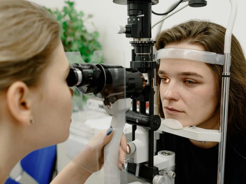 An eye doctor examines a woman's eyes using a slit lamp biomicroscope during an eye check-up.
