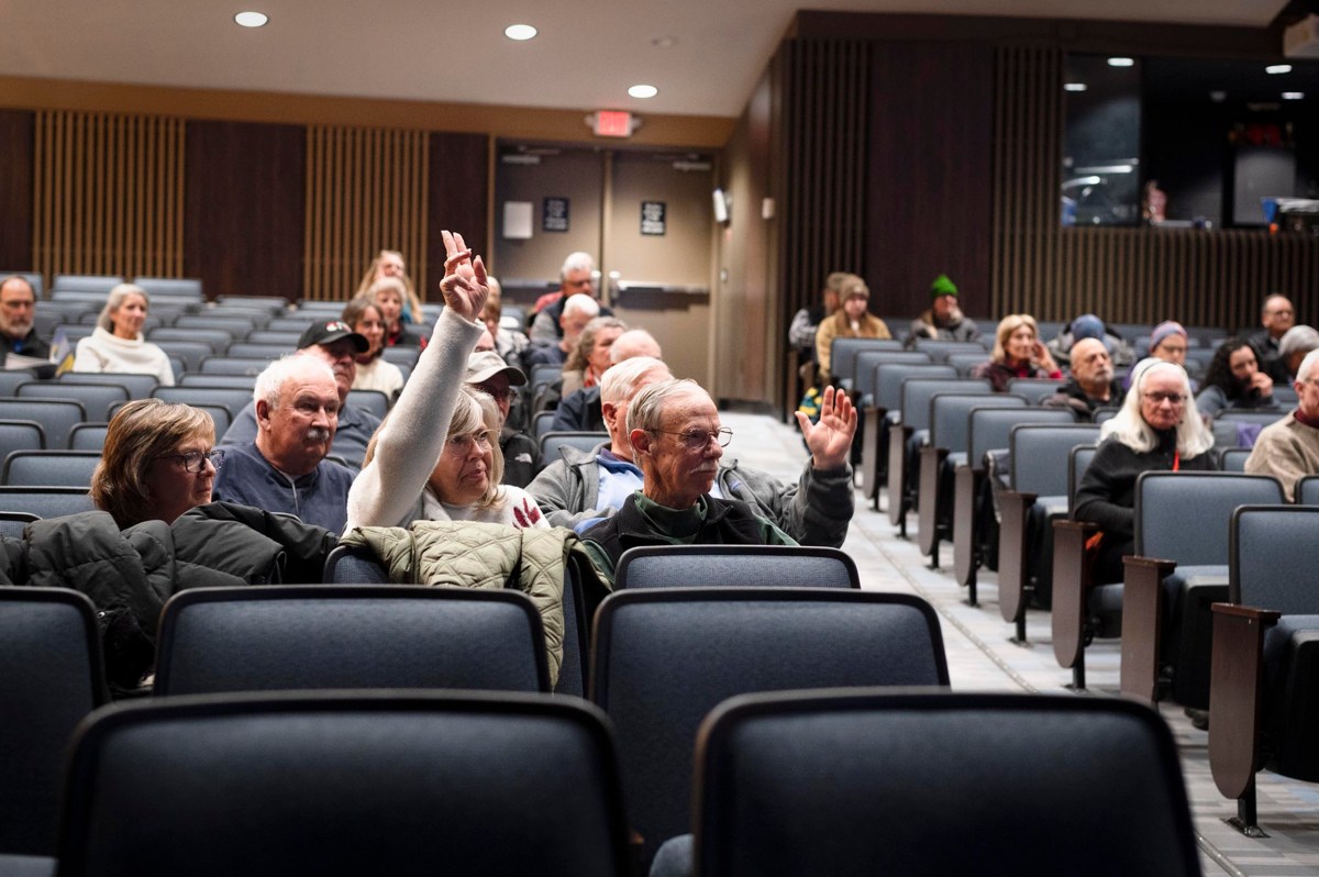 People seated in an auditorium, with two individuals in the foreground raising their hands, surrounded by others attentively listening.