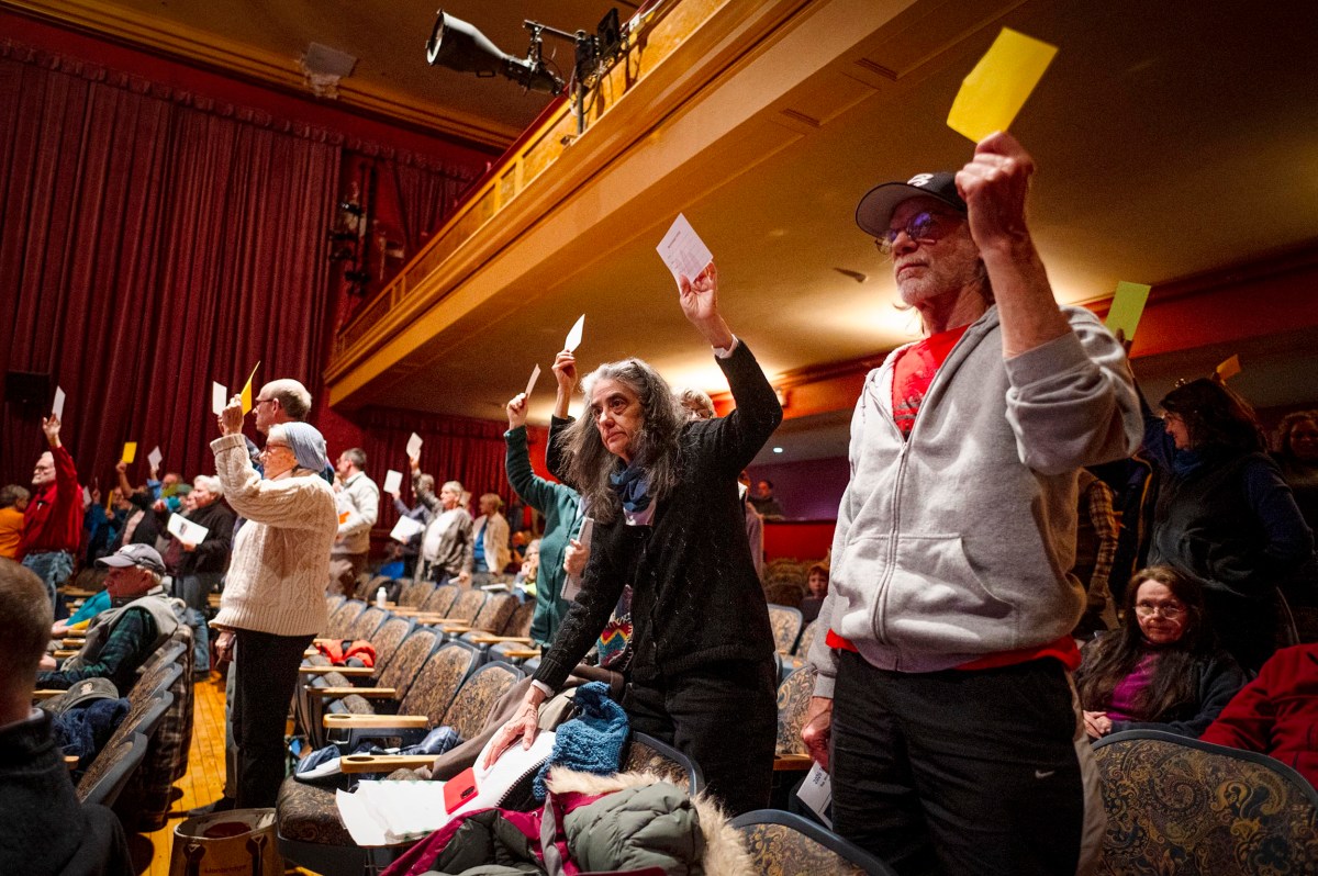A group of people standing in a theater, holding up yellow cards during what appears to be a vote or meeting.