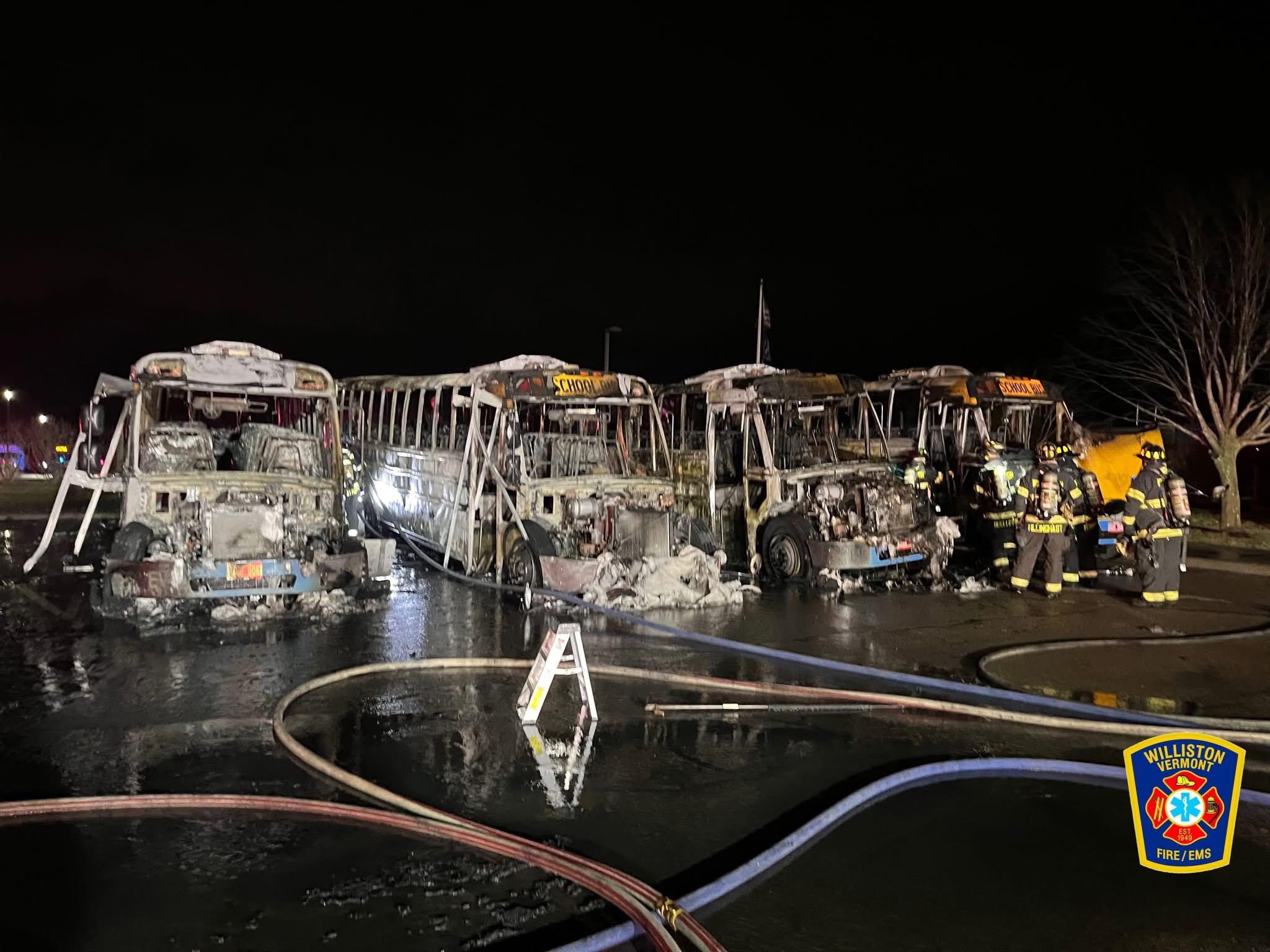 Several heavily burned school buses lined up at night, surrounded by firefighters and hoses; Williston Fire/EMS emblem is visible in the lower right corner.