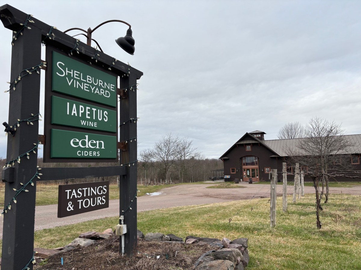 A wooden sign for Shelburne Vineyard advertises Iapetus wine, Eden ciders, and tastings and tours, with a barn-style building and vineyard in the background.