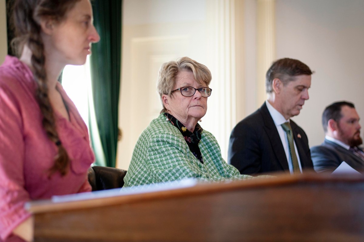 Four people sit at a table in a formal setting, focused and attentive, with documents in front of them.