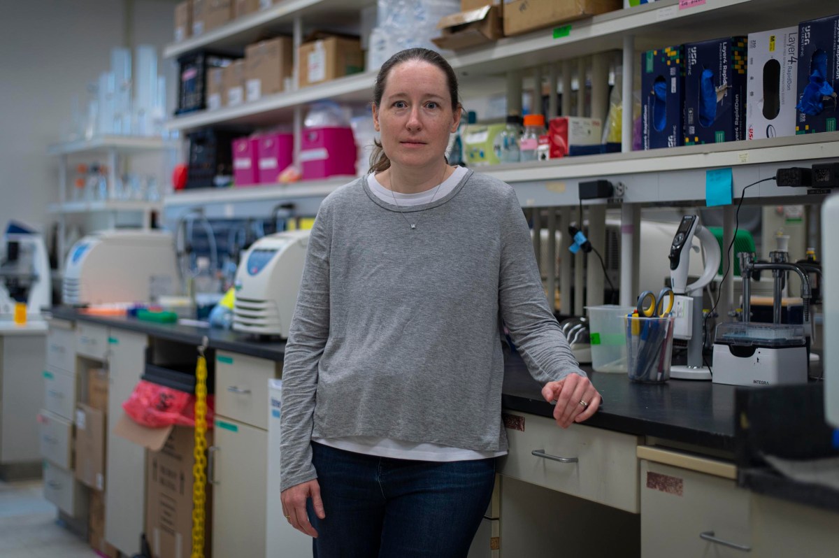 A woman stands in a laboratory, surrounded by scientific equipment, shelves with supplies, and workbenches.