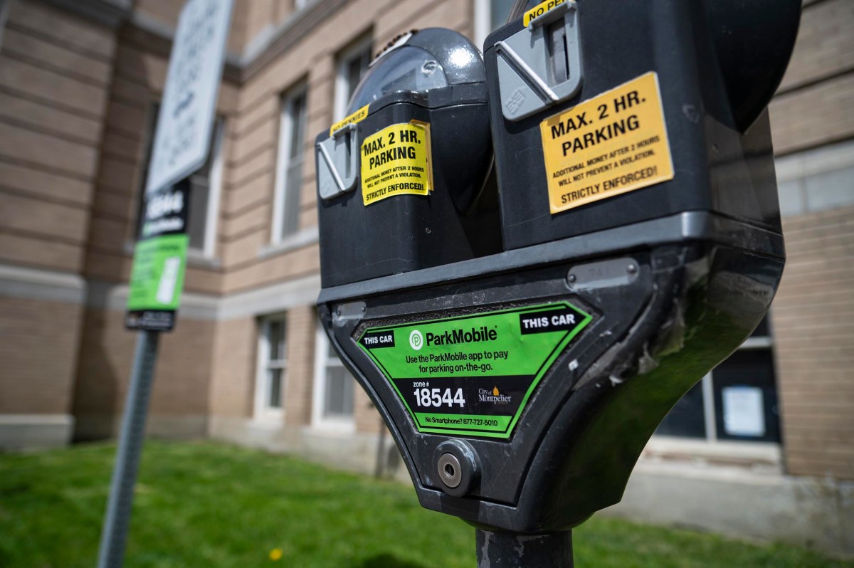 A close-up of a double-head parking meter labeled for a maximum of 2-hour parking, with ParkMobile payment information, outside a brick building.