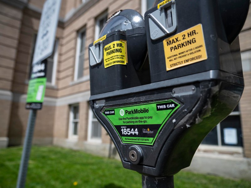 A close-up of a double-head parking meter labeled for a maximum of 2-hour parking, with ParkMobile payment information, outside a brick building.