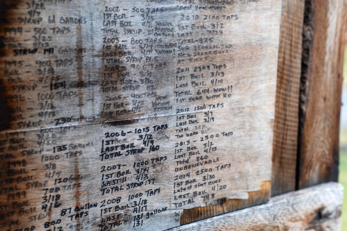 Handwritten lists of years, numbers, and notes are marked on a worn wooden board, possibly tracking maple syrup production or tree tapping records.