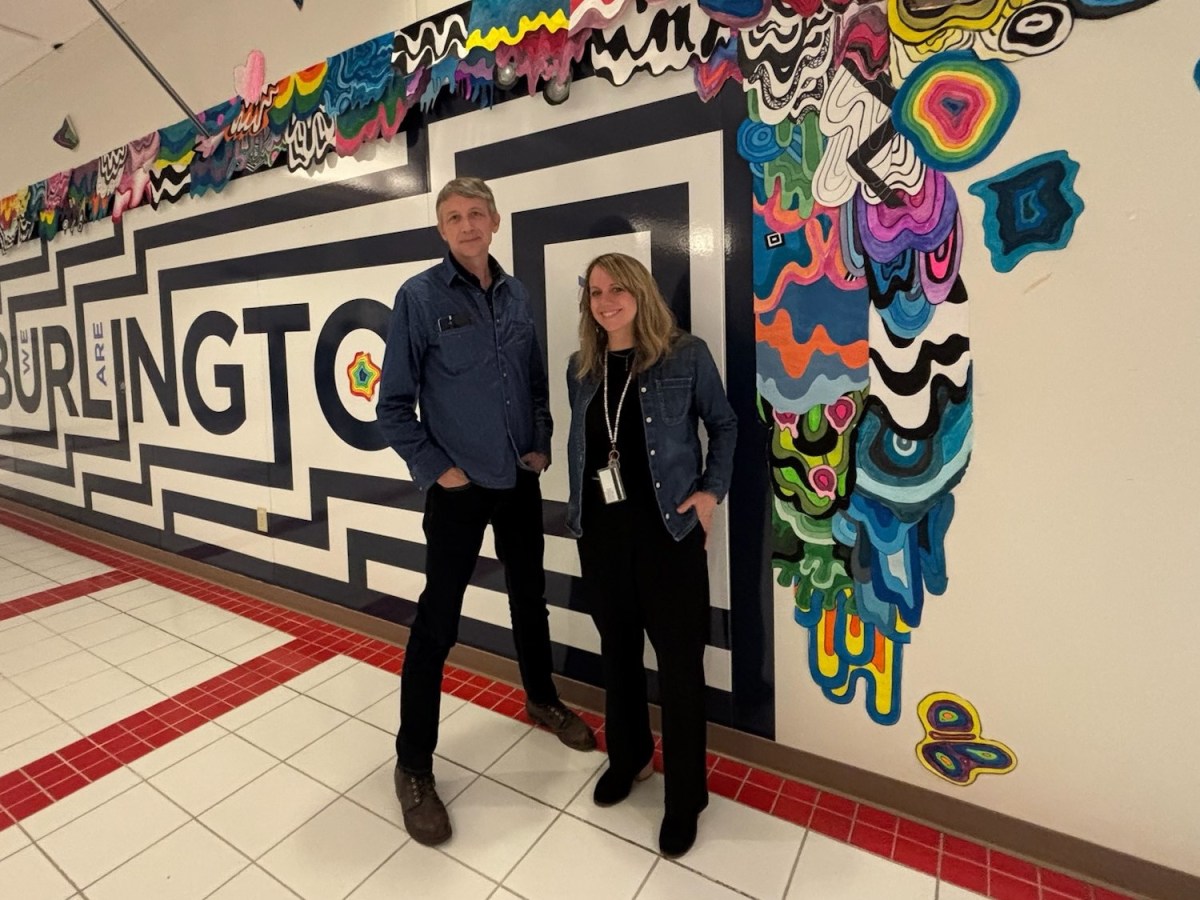 Two people stand in front of a wall mural with bold geometric patterns and colorful abstract shapes in a hallway labeled "BURLINGTON.