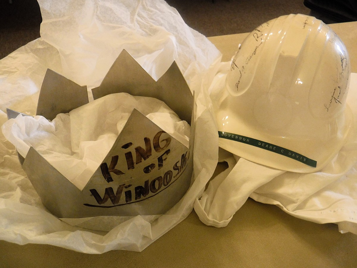 A metal crown labeled "King of Winooski" sits next to a signed white hard hat on a table with tissue paper.