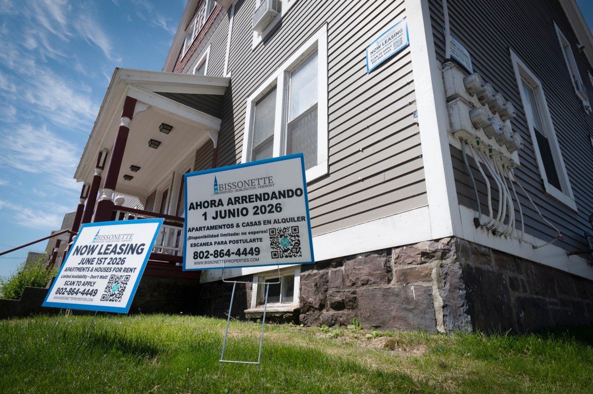 A residential building with signs on the lawn advertising apartment leasing in English and Spanish, with contact information and dates.