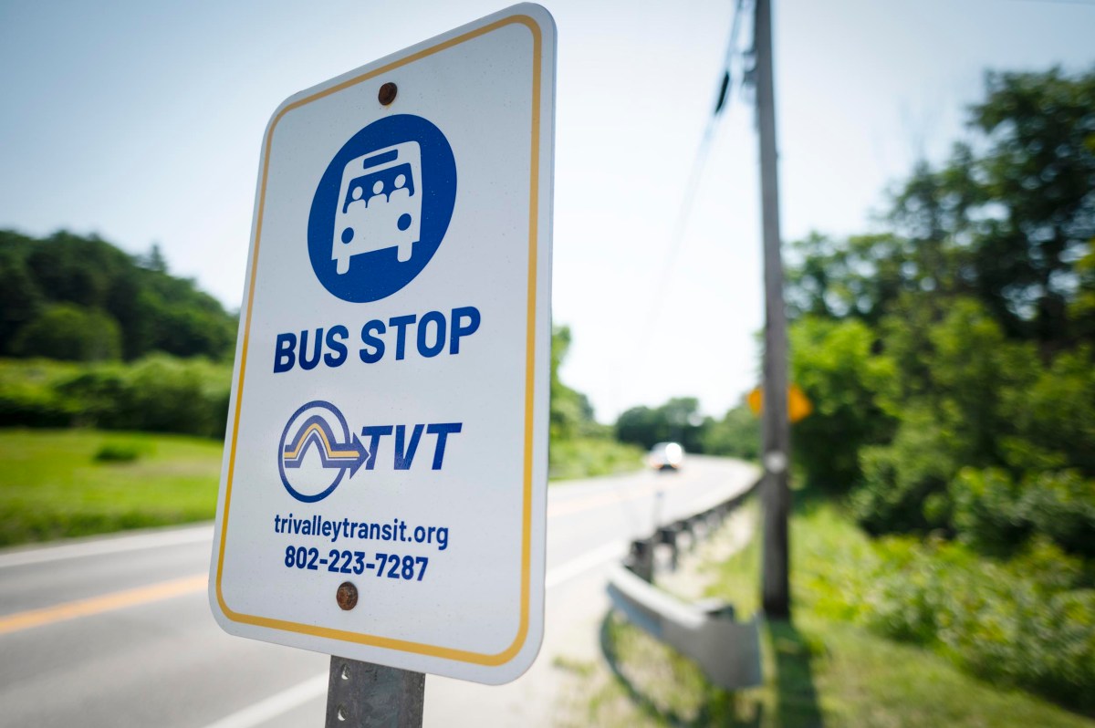 Close-up of a Tri-Valley Transit bus stop sign next to a rural road with trees and utility poles in the background.