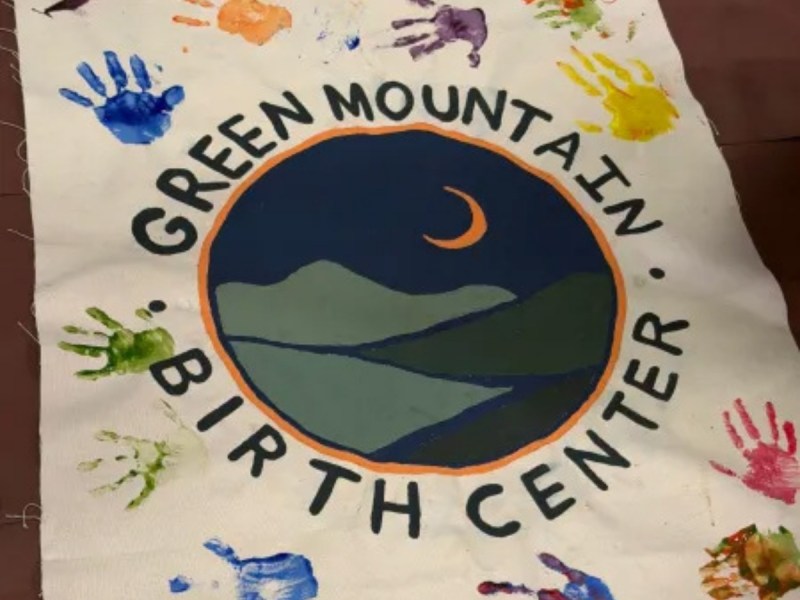 A cloth banner with a mountain logo and crescent moon, reading "Green Mountain Birth Center," surrounded by colorful painted handprints.