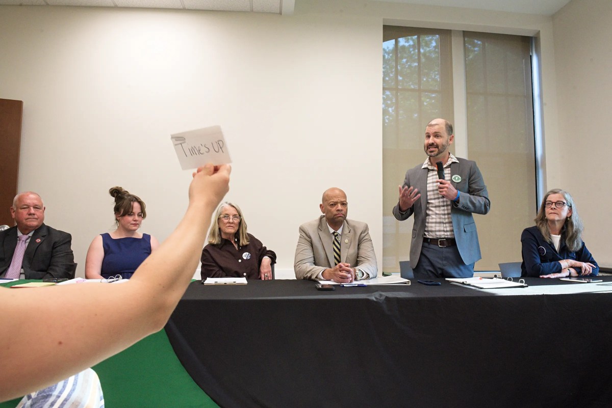 A person holds up a "TIME'S UP" card while a man speaks at a panel discussion with five seated panelists at a table.
