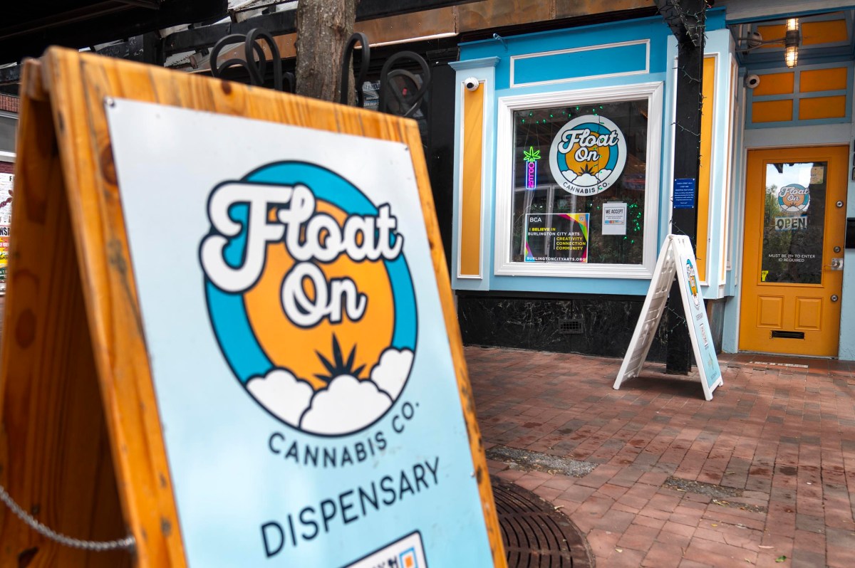 A cannabis dispensary storefront with "Float On" signs, colorful blue and orange decor, and a yellow door, seen from the sidewalk.