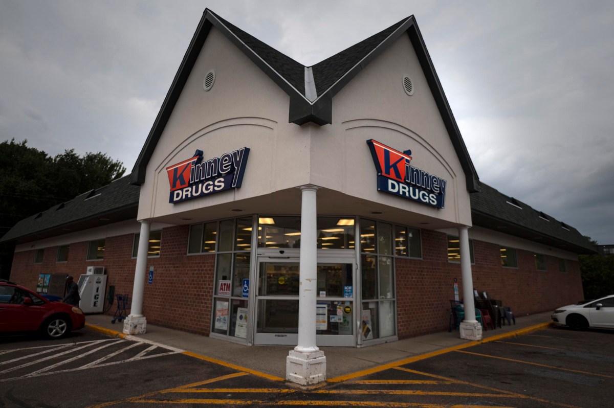 Exterior view of a Kinney Drugs store on a cloudy day, with glass entrance doors, parking spaces, and visible signs above the doorway.