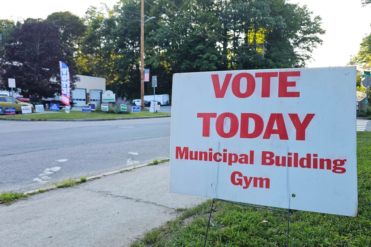 Large sign reads “VOTE TODAY Municipal Building Gym” near a road lined with election campaign signs and trees in the background.