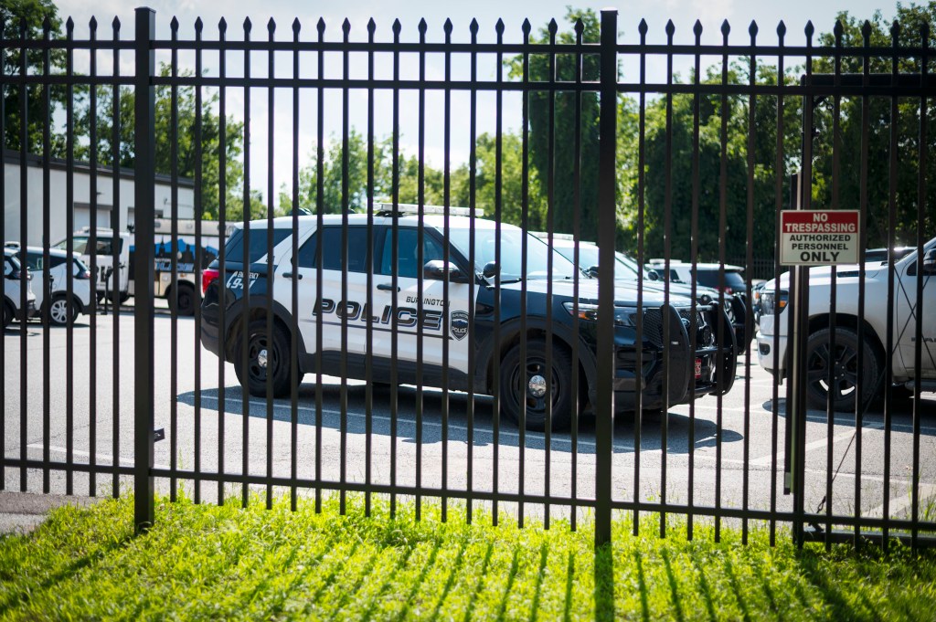 A police SUV is parked behind a black metal fence in a lot with other vehicles. A “No Trespassing Authorized Personnel Only” sign is posted on the fence.