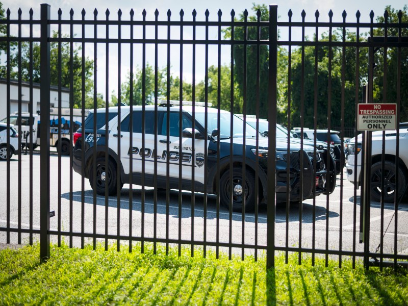 A police SUV is parked behind a black metal fence in a lot with other vehicles. A “No Trespassing Authorized Personnel Only” sign is posted on the fence.